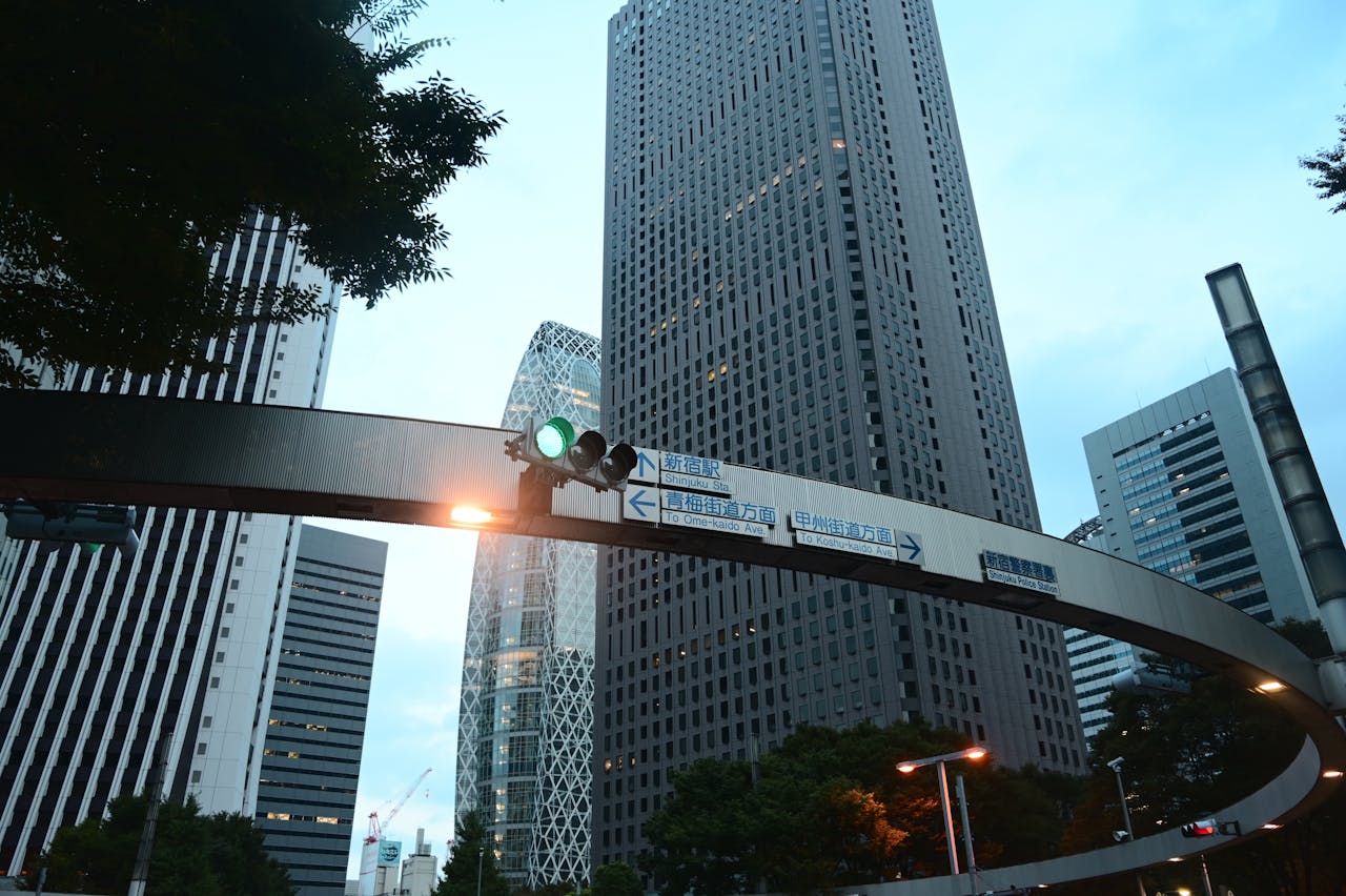 hero-img-01 Skyscrapers of Shinjuku, Tokyo captured at dusk with a prominent traffic signal and directional signs.